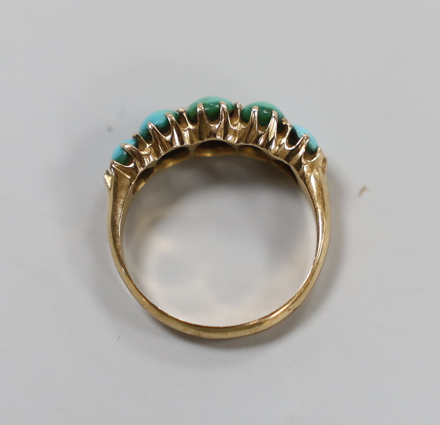 A yellow metal and graduated five stone cabochon turquoise set half hoop ring, size G/H, gross weight 2.4 grams.